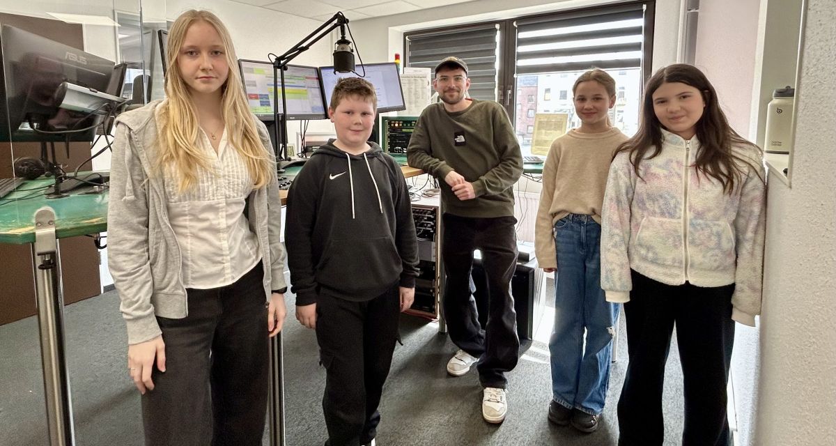 Zu sehen sind vier Schüler_inne im Studio B mit dem Moderator 