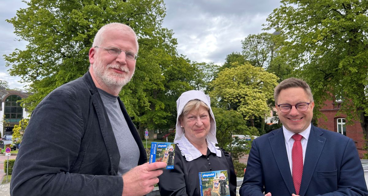 Die Playmobil-Figur von Maria von Jever wird vorgestellt. Mit dem verpackten Spielzeug in der Hand sind zu sehen (von links): Dr. Matthias Bollmeyer (Ratsmitglied und Initiator), Elisabeth Wilken als Fräulein Maria und Bürgermeister Jan Edo Albers.