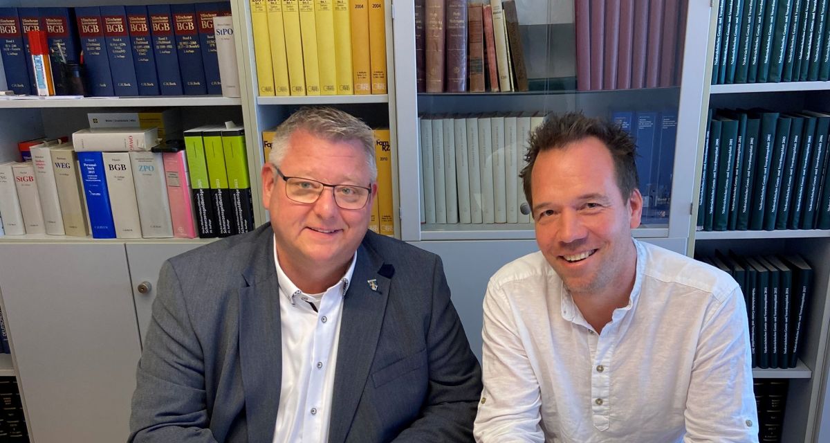 Wangerlands Bürgermeister Mario Szlezak und der Unternehmer Dirk Boll, Geschäftsführer der Abenteuerinsel GmbH unterzeichnen gut gelaunt den Kaufvertrag für die Rundinsel im Wangermeer. Sie sitzen in einem grauen Büro, im Hintergrund stehen Bücher in Regalen. 
