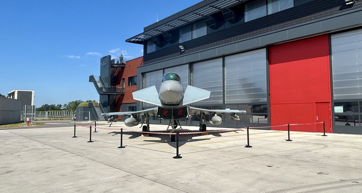 Zu sehen ist ein unbesetzter Kampfjet Eurofighter vor einer Halle von vorn. Das rote R des Geschwaders ist deutlich sichtbar.
