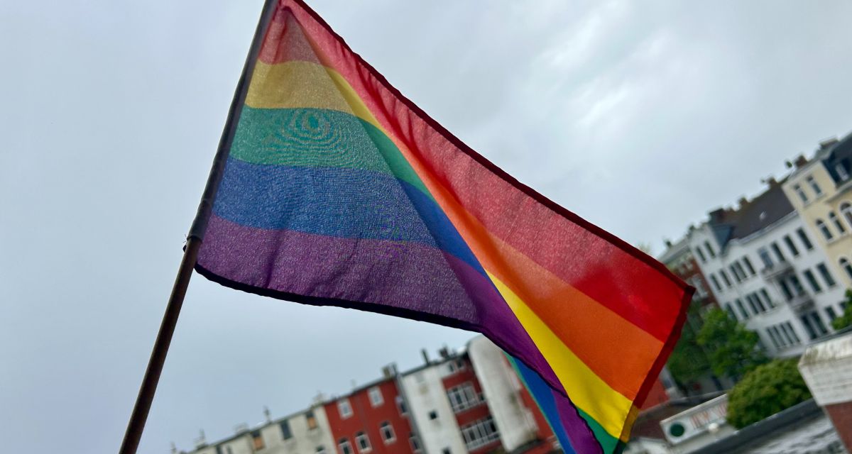 Prideflagge vor Wilhelmshavener Fassaden an wolkigem Tag