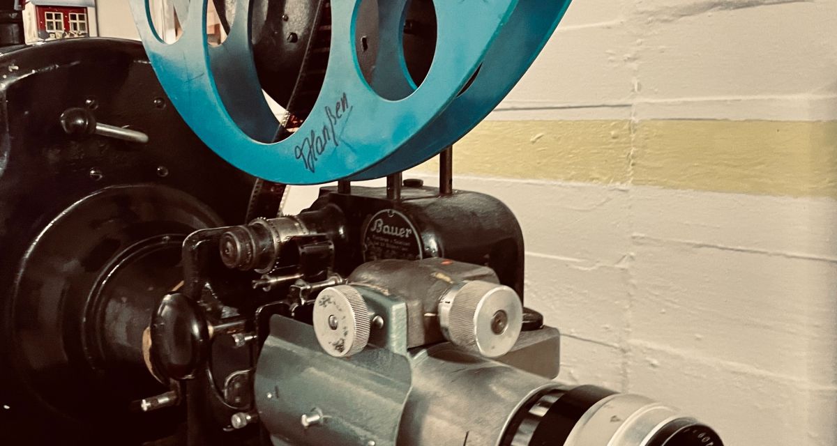 Zu sehen sit ein Foilmprojektor von schräg vorne vor gekalkter Wand.