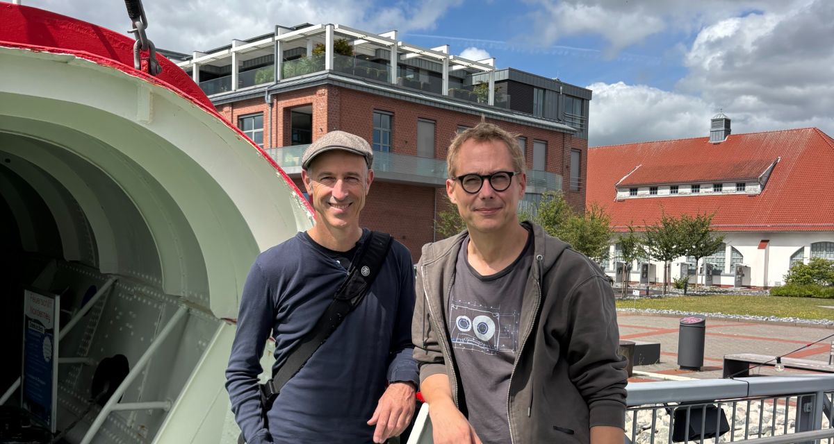 Zu sehen sind an Ddeck des Feuerschiffs Norderney Regisseuer Michael Uhl und Ausstatter Thomas Rump. Das Wetter ist sonnig, im Hintergrund ist das TheOs zu sehen.