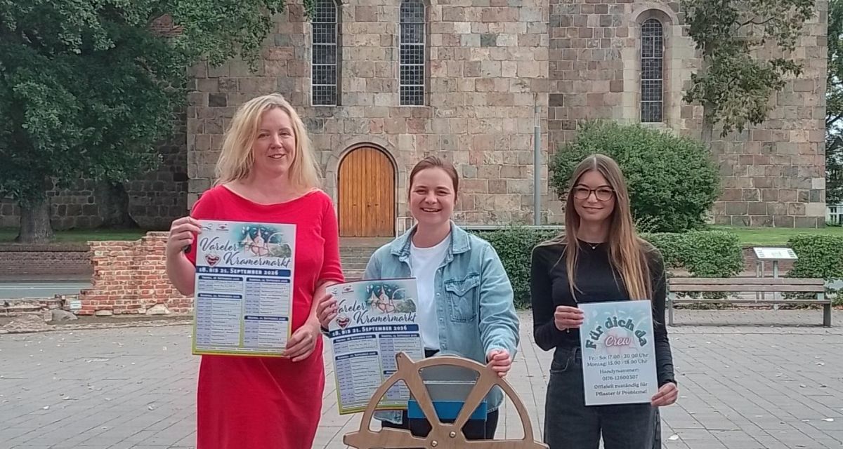Dr. Meike Knop (Wirtschaftsförderung), Yvonne Uhr (Marktmeisterin) und Noémie Fernandez (Jugendzentrum Weberei) präsentieren vor der Schlosskirche in Varel das Plakat für den 259. Kramermarkt.