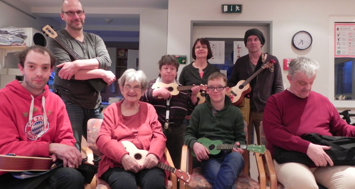 Mehrere Menschen unterschiedlichen Alters posieren mit Ukulelen für die Kamera.