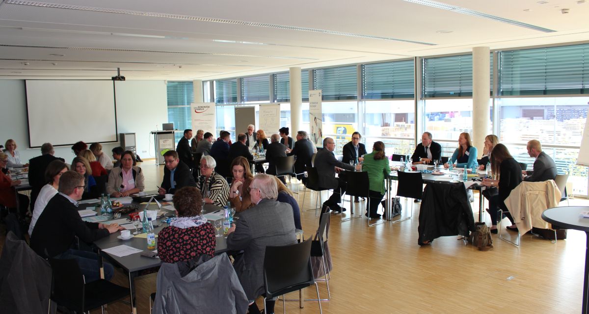 Mehrere Menschen bilden an diversen Tischen Arbeitsgruppen.