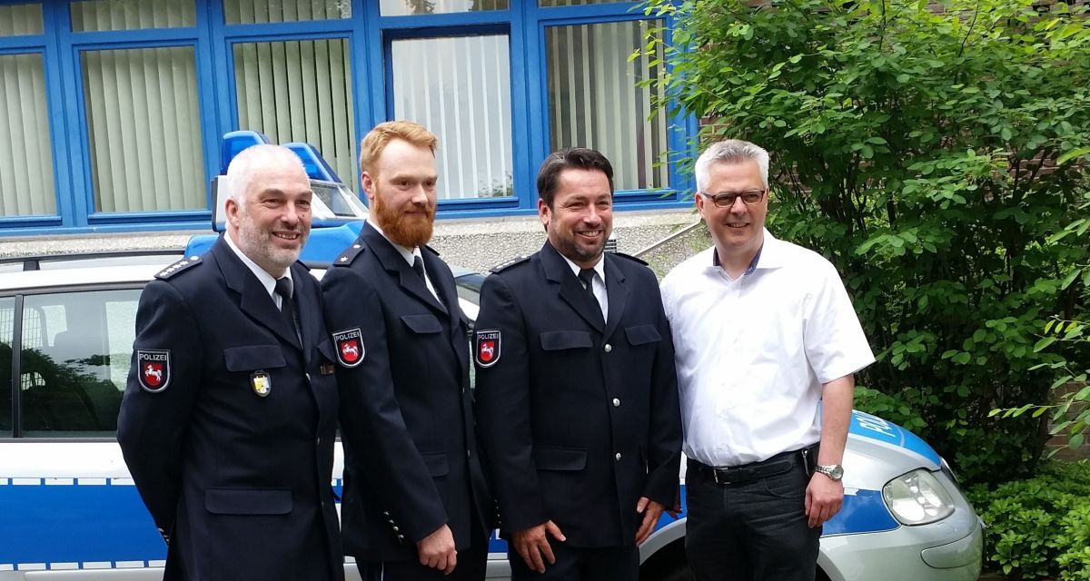 Drei Polizisten und ein Bürgermeister lächeln in die Kamera. Hinter ihnen ein Streifenwagen.