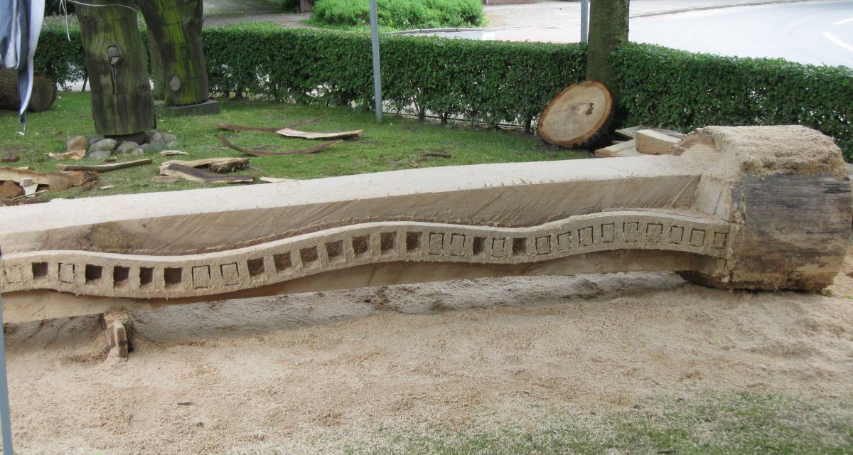 Zu sehen ist eine abstrakte Holzskulptur am Boden liegend.