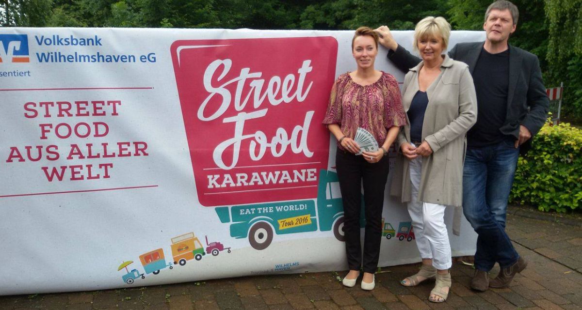 Drei Menschen, unter anderem WTF - Geschäftsführer Michael Diers stehen vor einem Plakat der 