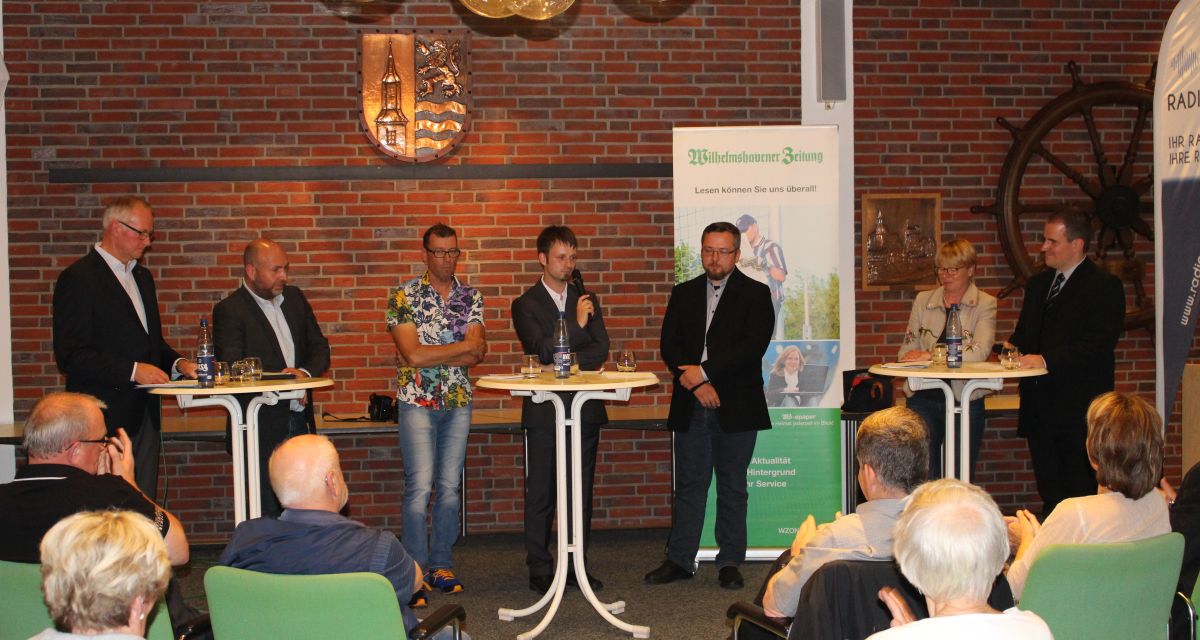 Zu sehen sind verschiedene Redner und ein Publikum bei einer Podiumsdiskussion im Rathaus in Sande.