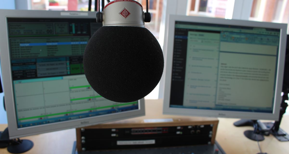 Ein großes Kugelmikrophon hängt vor zwei Computerbildschirmen.