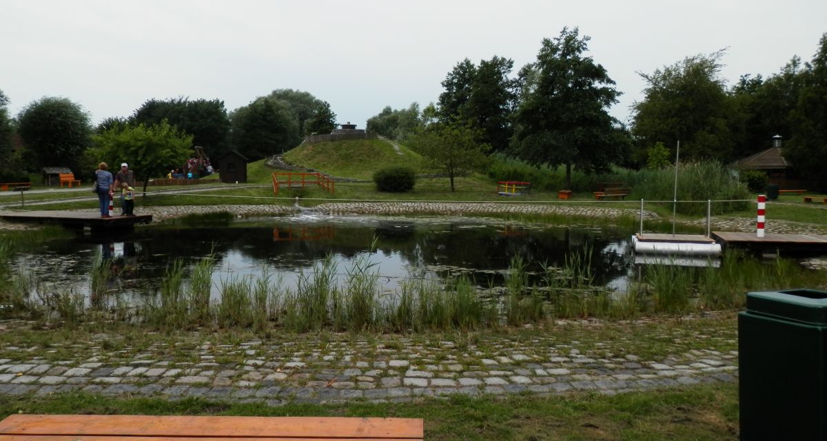 Man sieht einen kleinen Teich mit Sitzbänken umzu.