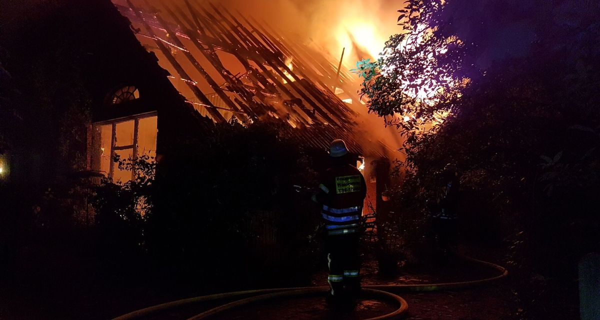 Zu sehen ist ein brennendes Einfamilienhaus im Wangerland und eine Feuerwehrkraft