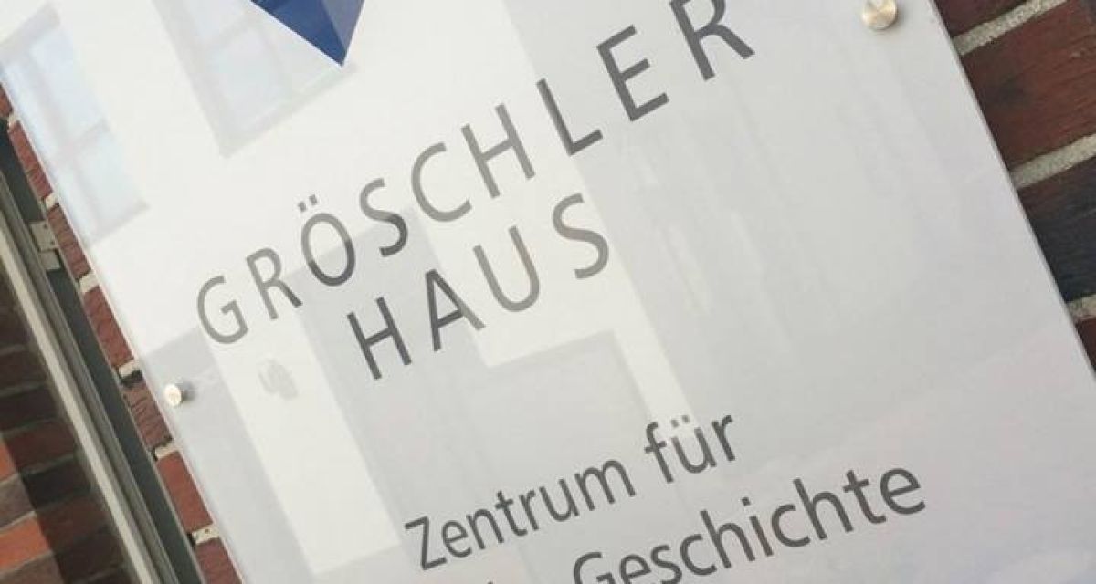 Auf dem Bild ist das Schild mit Logo vom GröschlerHaus in Jever zu sehen. Unter dem Logo und Schriftzug steht 