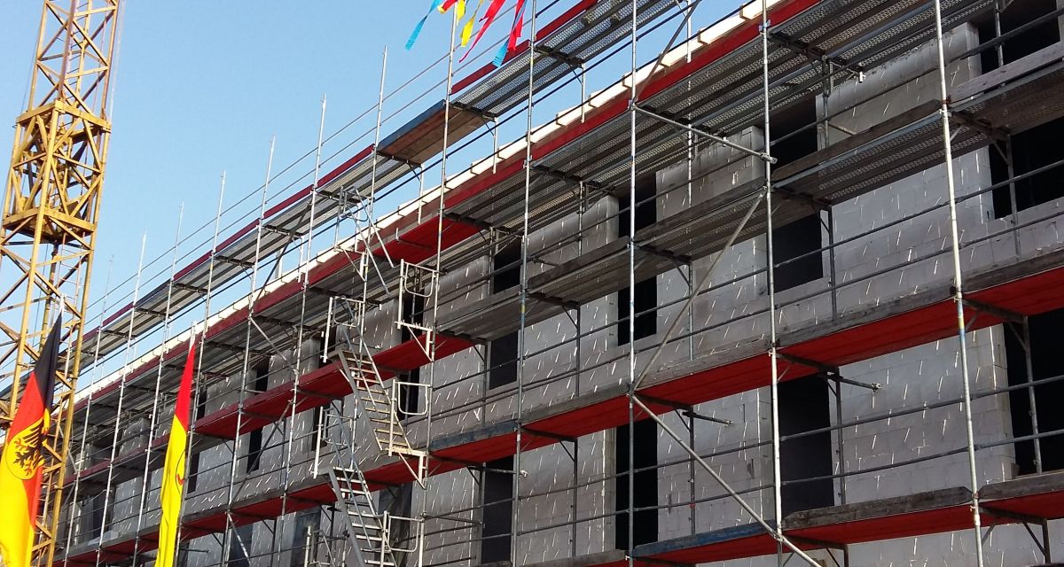 Ein Kran hebt einen Richtkranz auf einen Neubau