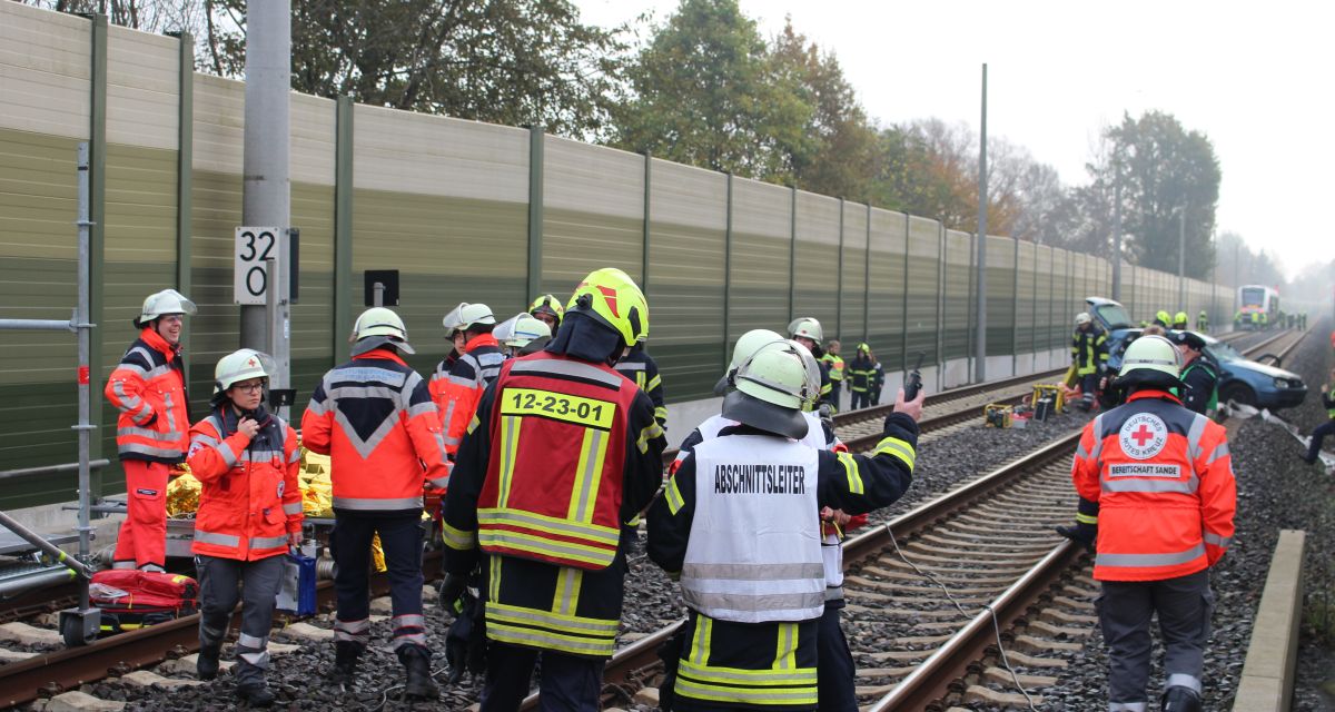 Rettungskräfte stehen auf Bahngleisen. Ein Zug ist mit einem Auto kollidiert. Es handelt sich aber um eine Übung.