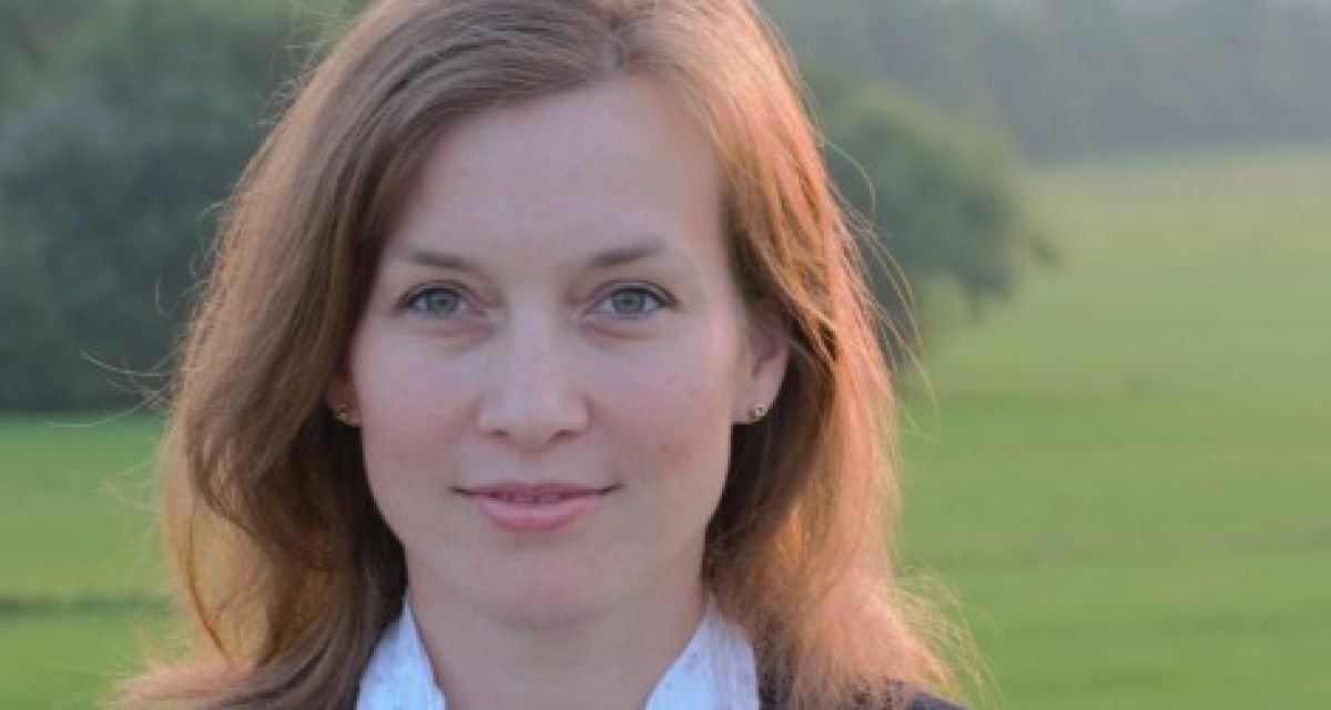 Eine Frau mit rot-braunnen Haaren vor einer Wiesenlandschaft