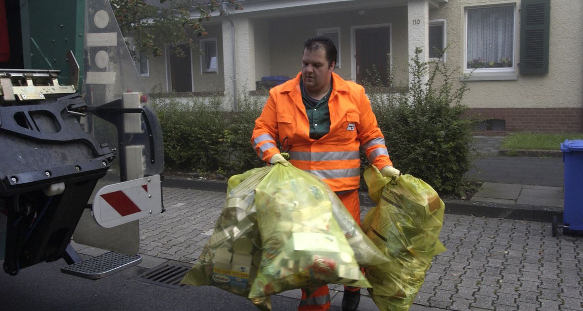 Ein Mitarbeiter eines Abfallwirtschaftsbetriebs trägt gelbe Säcke zum Müllfahrzeug.
