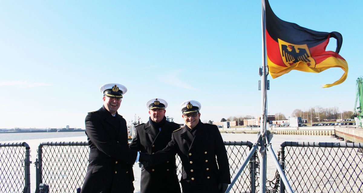 Drei Männer in Mänteln und Kapitänsmützen schütteln sich die Hände.