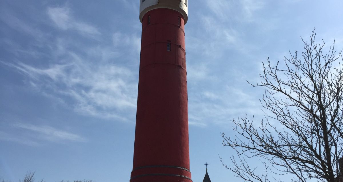Zu sehen ist der alte Leuchtturm von Wangerooge: er ist größtenteils rot, der obere Teil ist weiß.