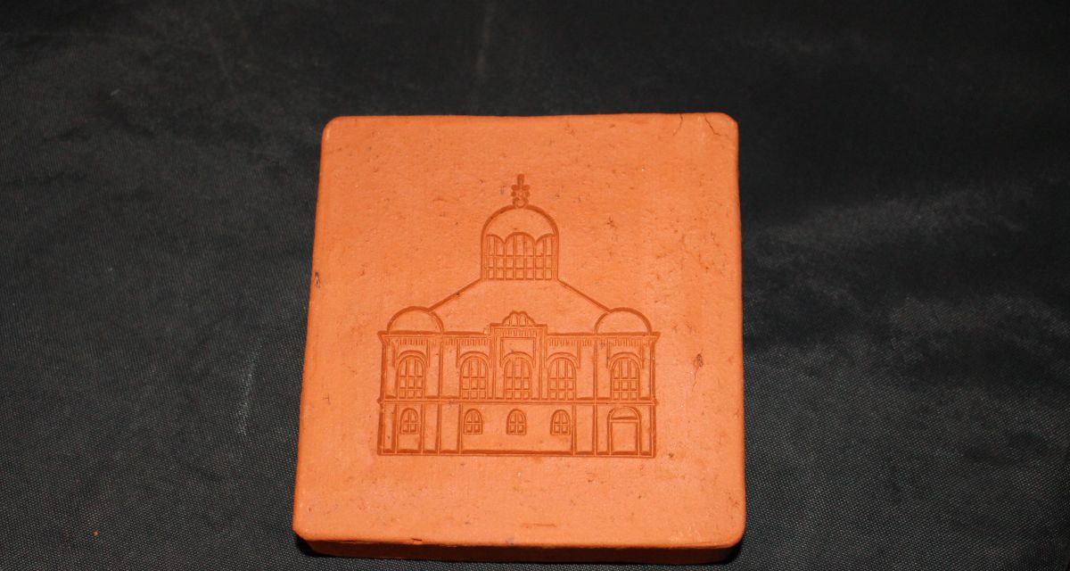 Auf dem Foto ist ein Gedenkziegelstein für eine Synagoge zu sehen. In dem roten Stein ist das Bild einer Synagoge eingeprägt.