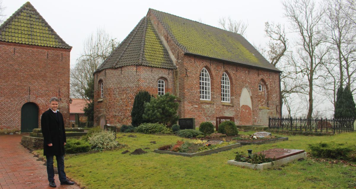 Pastor Grünefeld steht neben einer Kirche. 