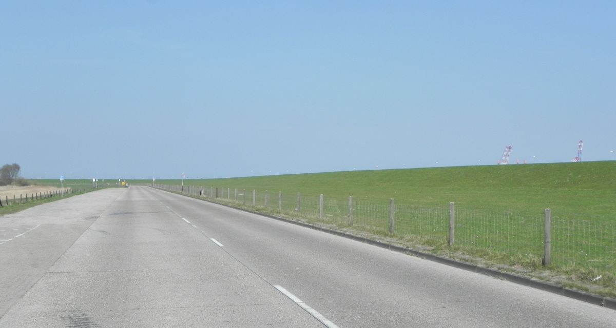 Graue Straße verläuft vor dem Deich.