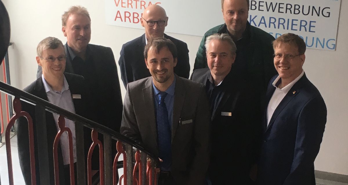 Männer im Anzug stehen auf einer Treppe im Jobcenter. Sie sind alle Partner im Fachkräftebündnis JadeBay