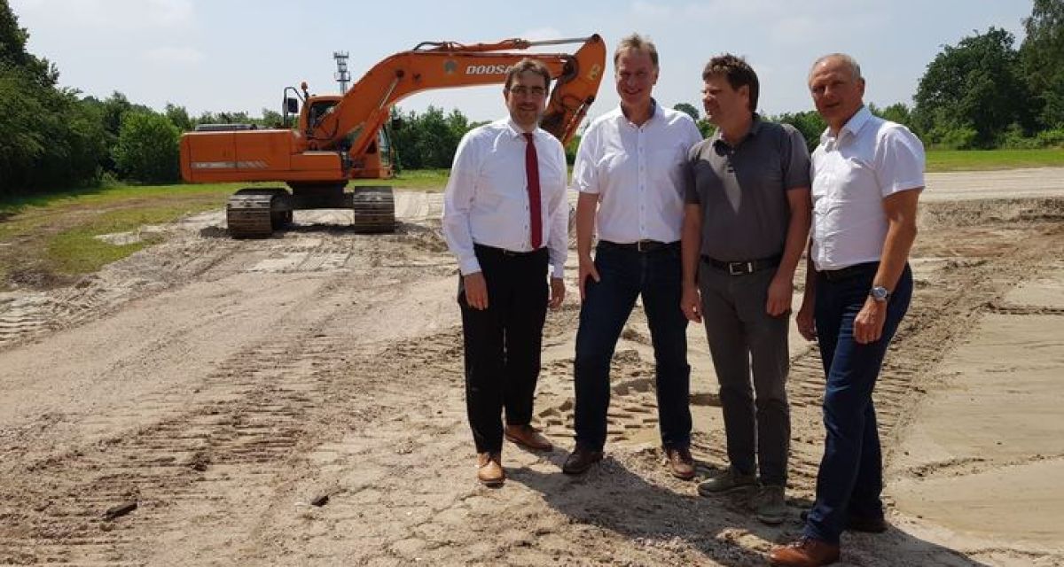 Vier Menschen stehen vor einem Bagger und freuen sich über den Beginn der Bauarbeiten bei Deutsche Windguard