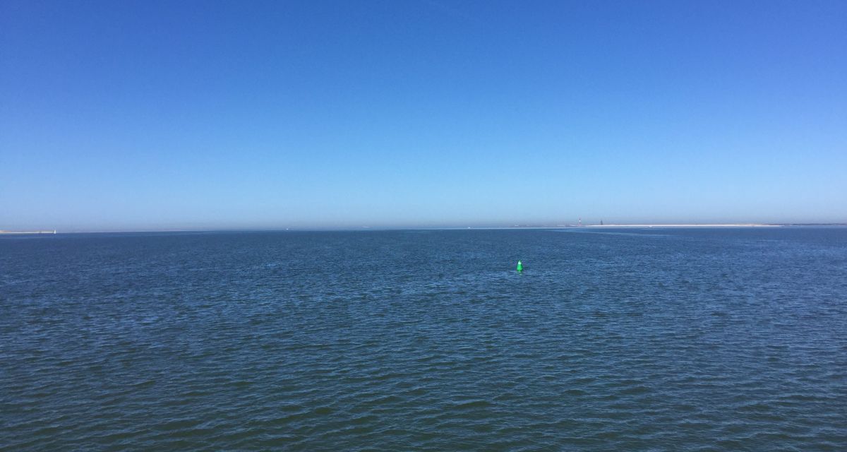Zu sehen ist eine ruhige blaue Nordsee unter blauem Himmel.