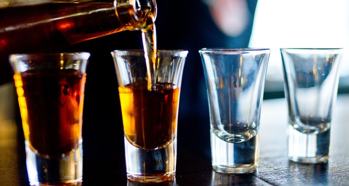 Schnapsgläser werden aus einer Flasche mit einer braunen Flüssigkeit befüllt