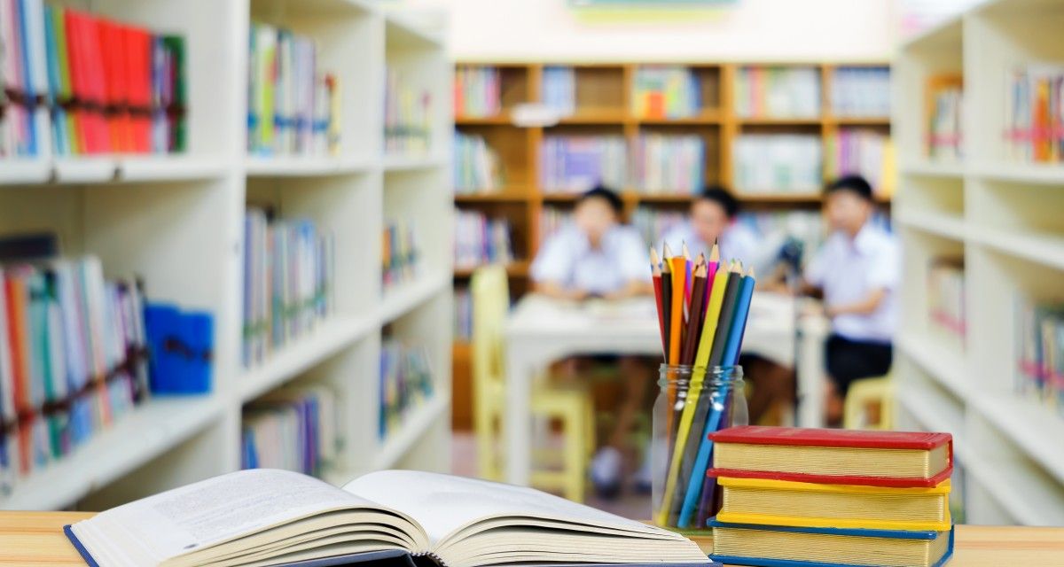 Buch, Stifte, Bücher, Bibliothek im Hintergrung unscharf Kinder Symbolbild für Schule