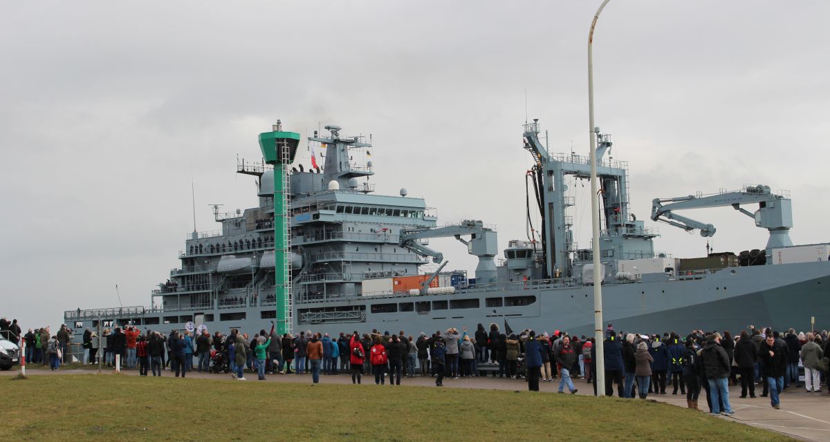 Acht Männer der Feuerwehr Wilhelmshaven stehen vor Feuerwehrfahrzeugen zusammen mit Oberbürgermeister Carsten Feist