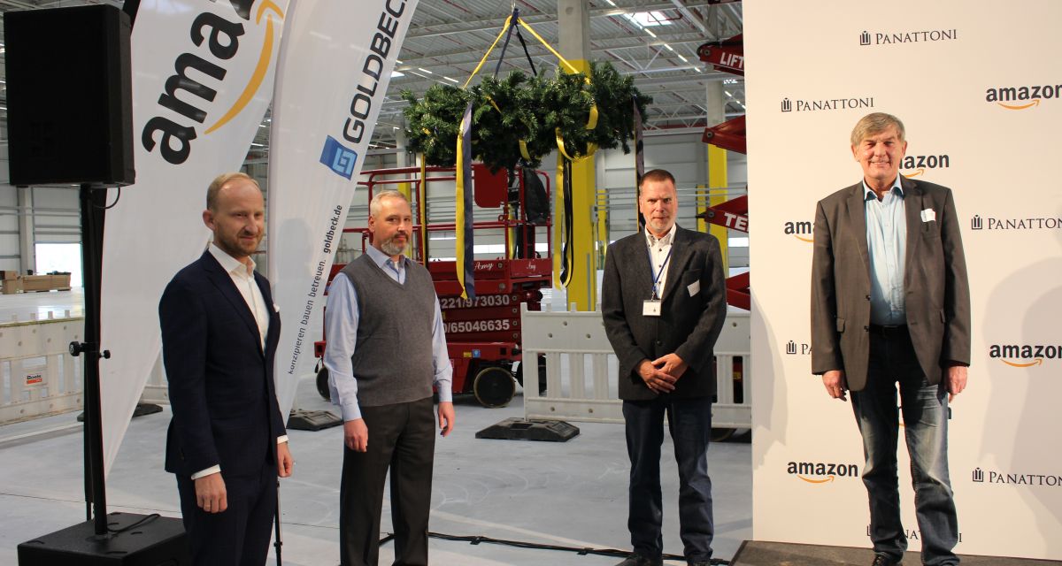 Richtfest im Amazon Verteilzentrum. Vier Vertreter unter anderem Schortens Bürgermeister Gerhard Böhling stehen in einer großen Halle vor Aufstellern.