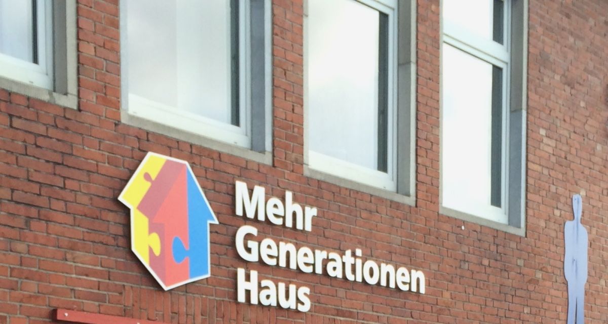 Zu sehen ist die Gebäudefront des Mehrgenerationenhauses an der Banter Kirche in Wilhelmshaven. Das Gebäude ist aus Rotklinker gebaut, unter den Fenstern ist das gelb-rot-blaue Logo und der Schriftzug 