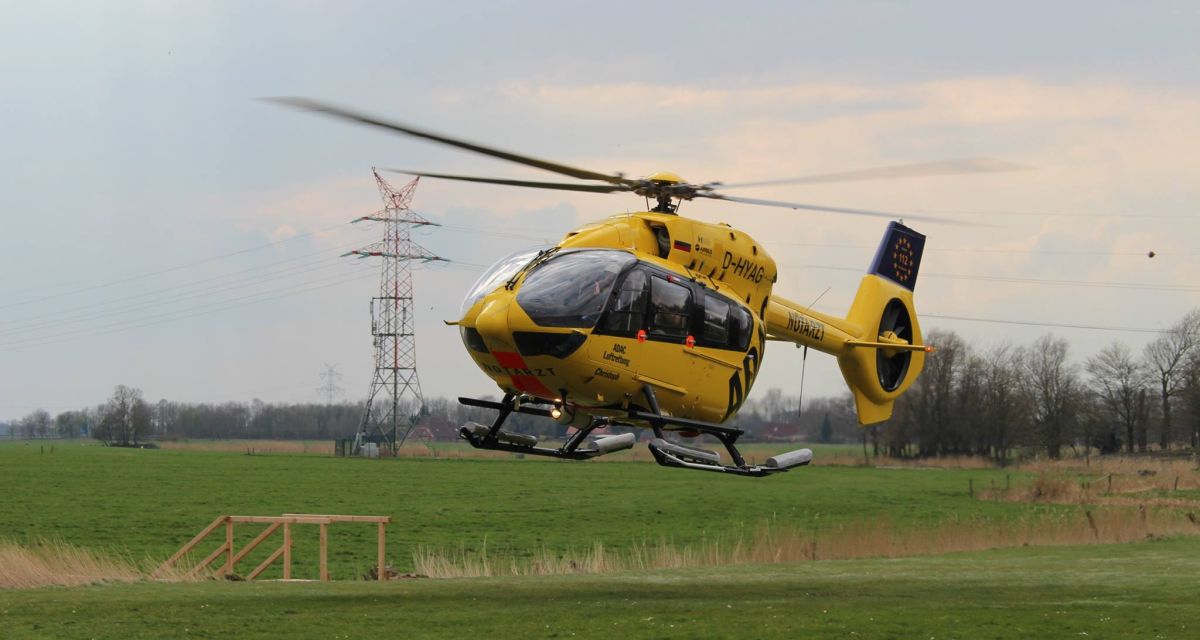 Ein gelber Hubschrauber bei der Landung auf einer grünen Wiese. Christoph 26 