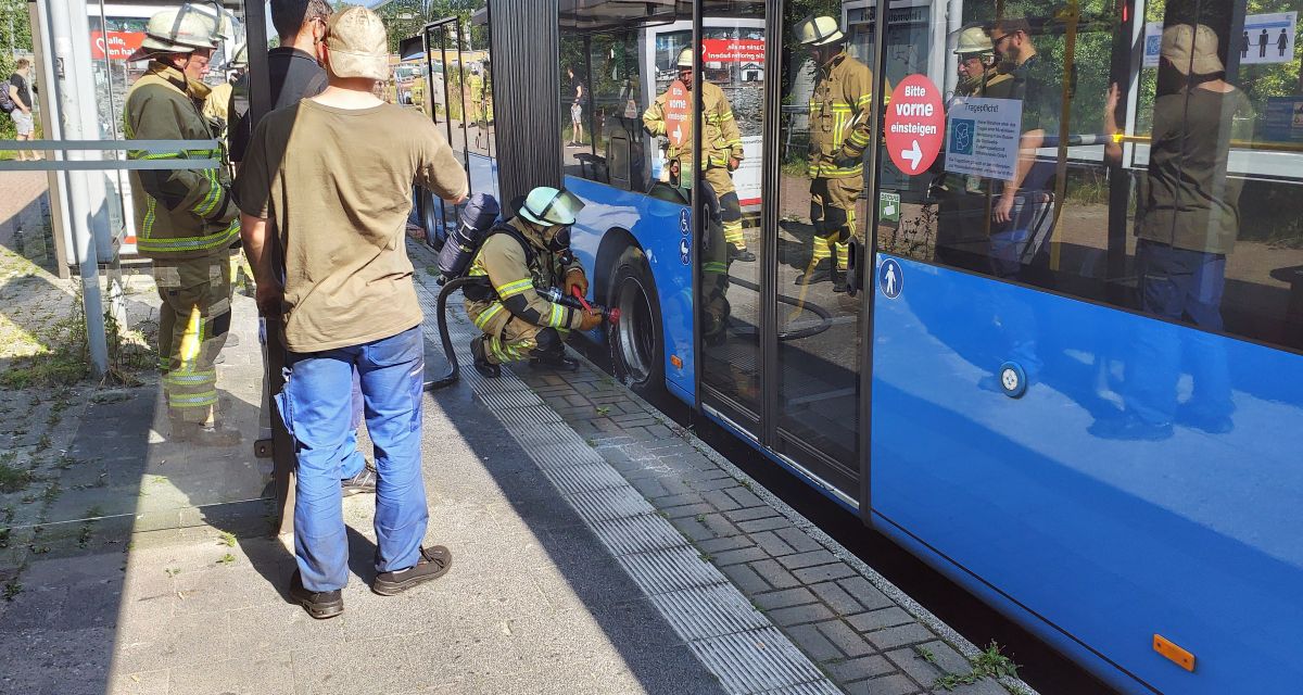 Viele Menschen und Feuerwehrleute stehen um einen Bus der Stadtwerke Wilhelmshaven. Überhitzte Bremsen werden gekühlt.
