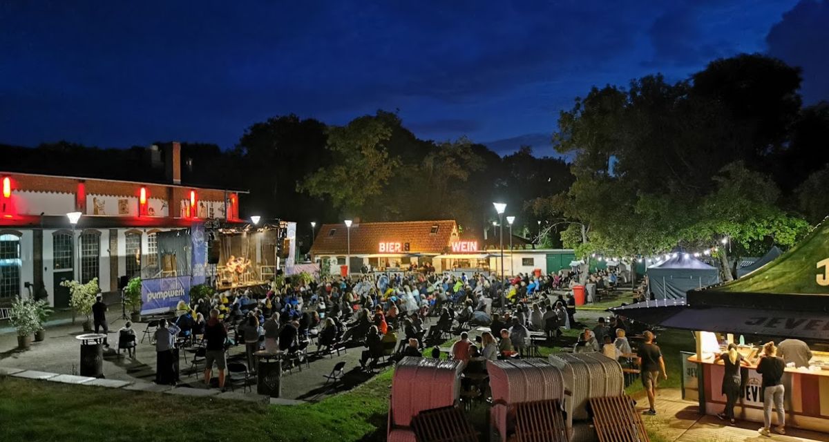 Auf dem Bild ist das Pumpwerk bei Nacht zu sehen. Auf einer Open Air Bühne spielt ein Konzert, eine große Menschenmenge schaut zu. 