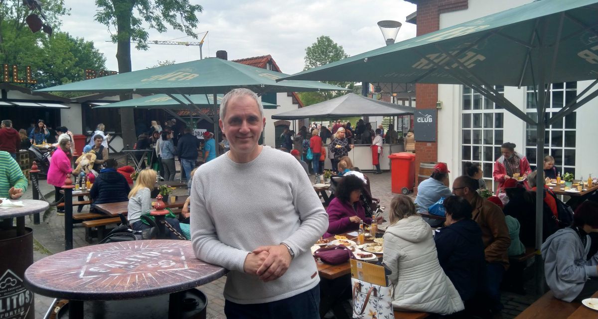 Reinhard Päsler vom Migrationsbüro Wilhelmshaven steht vor gut besetzten Bierbänken am Pumpwerk im Rahmen des Willkommensfestes für Geflüchtete aus der Ukraine