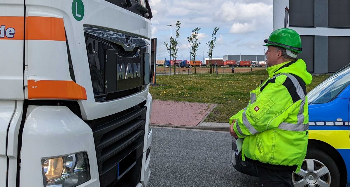 Warnstreik der Dienstleistungsgewerkschaft ver.di am JadeWeserPort. Ein Beschäftigter in Warnwest und Schutzhelm steht mit verschränkten Armen vor einem Lkw und hält den Verkehr auf.