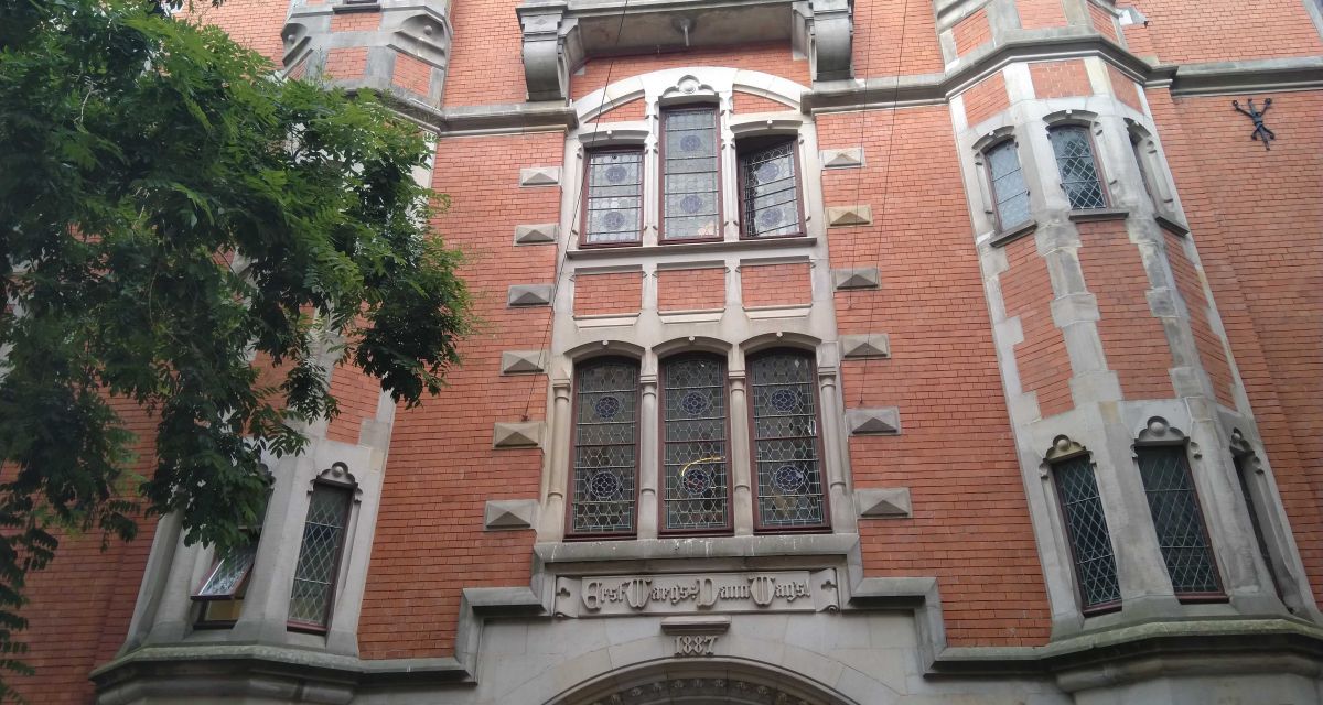 Das historische Rathaus der Stadt Oldenburg. Ein mehrgeschossiges Gebäude aus Rotklinker mit Sandsteinabsetzungen und Bleiglasfenstern. Über dem Portal steht der Wahlspruch 