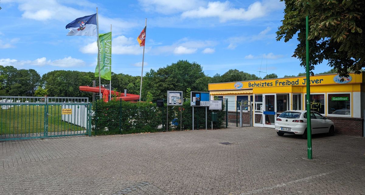 Das Freibad Jever mit Eingangsbereich und Parkplatz bei Sonnenschein