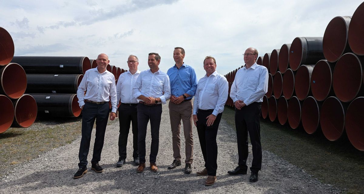 Beim Baustart für die Wilhelmshavener Anschlussleitung WAL vom künftigen LNG-Terminal Wilhelmshaven nach Etzel stehen (v.l.n.r.): Torben Kleinfeldt (Friedrich Vorwerk Group), Thomas Jung (Max Streicher GmbH), Umwelt- und Energieminister Olaf Lies (SPD), Thomas Hüwener (OGE), Friedeburgs Bürgermeister Helfried Götz und Christian Boppert (Mannesmann Großrohr GmbH) zwischen den aufgeschichteten Rohrleitungen.