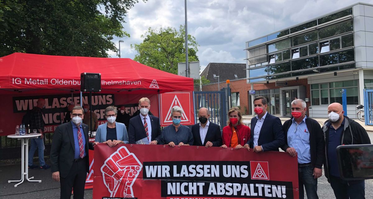 Zu sehen sind politische Vertreter*innen mit einem Banner, auf dem für das Werk Varel demonstriert wird. 