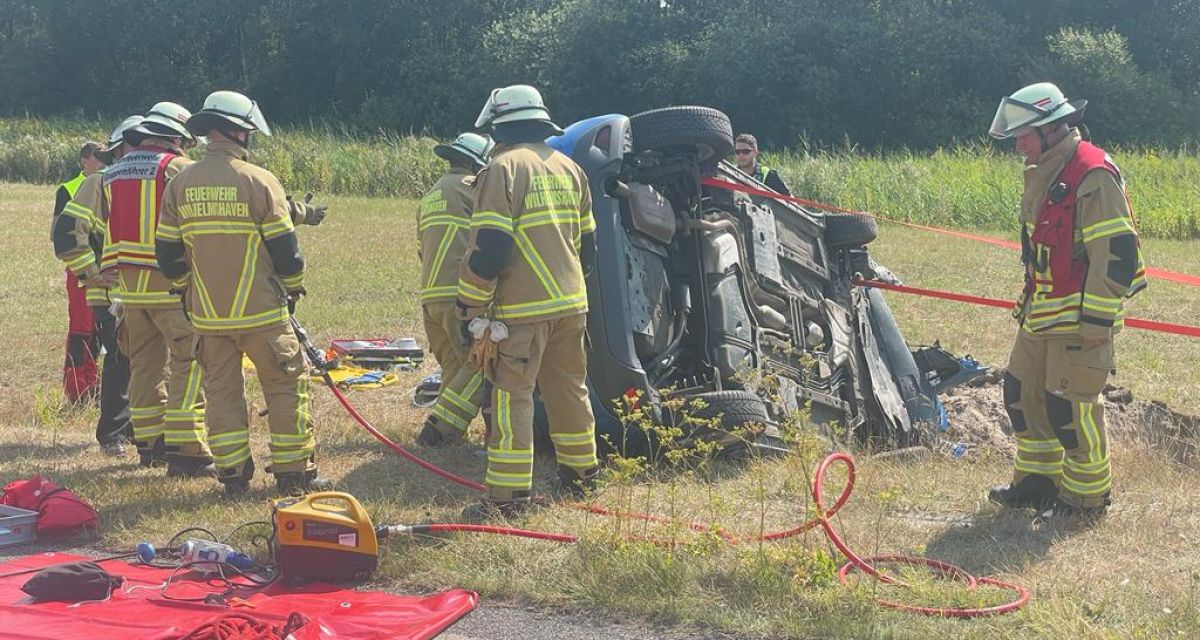 Mehrere Einsatzkräfte der Feuerwehr bergen ein Auto, das aktuell auf der Seite am Straßenrand liegt