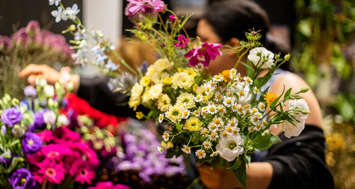 Eine Frau hält viele Blumen in der Hand, die sie vermutlich gerade für ein Blumengesteck aussucht