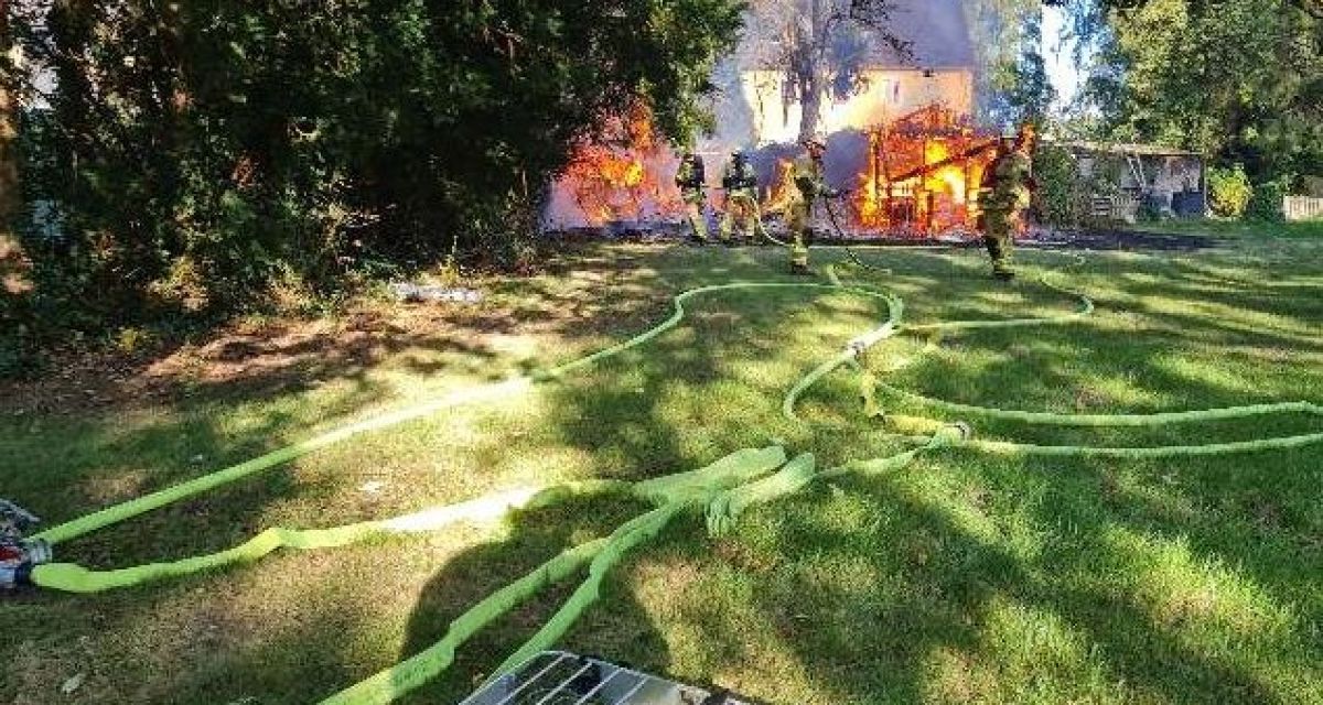 Zu sehen sind brennende Gartenhäuser, die von einigen Feuerwehrleuten gelöscht werden. 