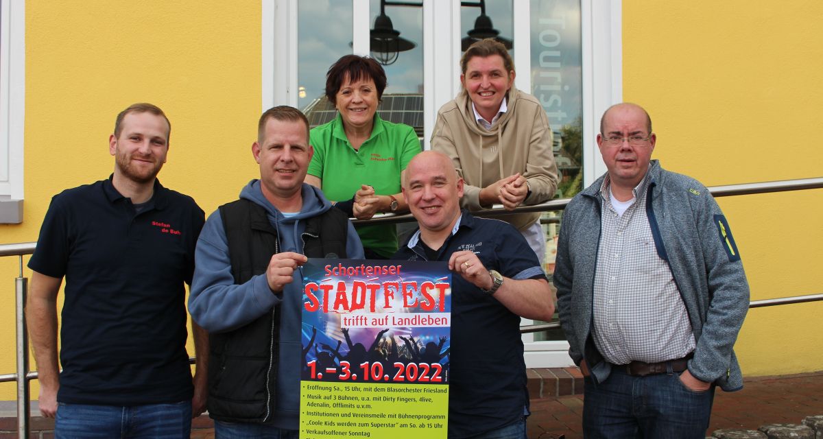 Stadtfest Schortens trifft auf Landleben. Mehhrere Menschen halten ein Plakat für die Veranstaltung hoch.