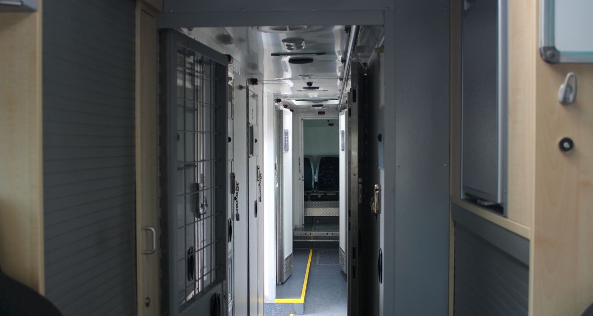 Im Gefängnisbus der JVA scheint Licht durch einen schmalen Gang, von dem die Transportzellen abgehen. 