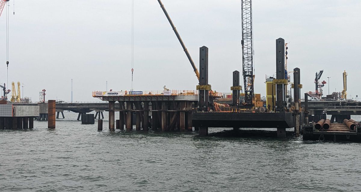 Eine LNG-PLattform bei grauem Regenwetter von Wasserseite aus. Viele Baugeräte befinden sich auf der Plattform